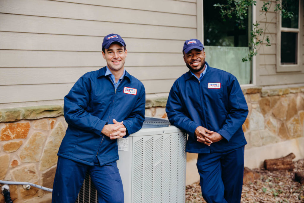 two technicians leaning on outdoor unit and smiling