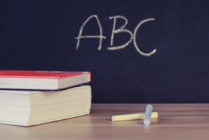 A chalkboard with the letters A, B, C written on it behind a desk with chalk and an HVAC glossary on it