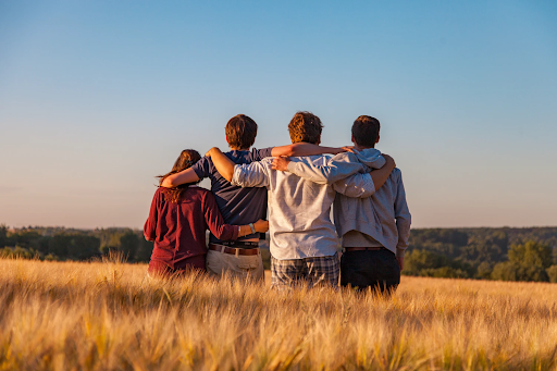 4 people holding each other's shoulders in a brown grassy field