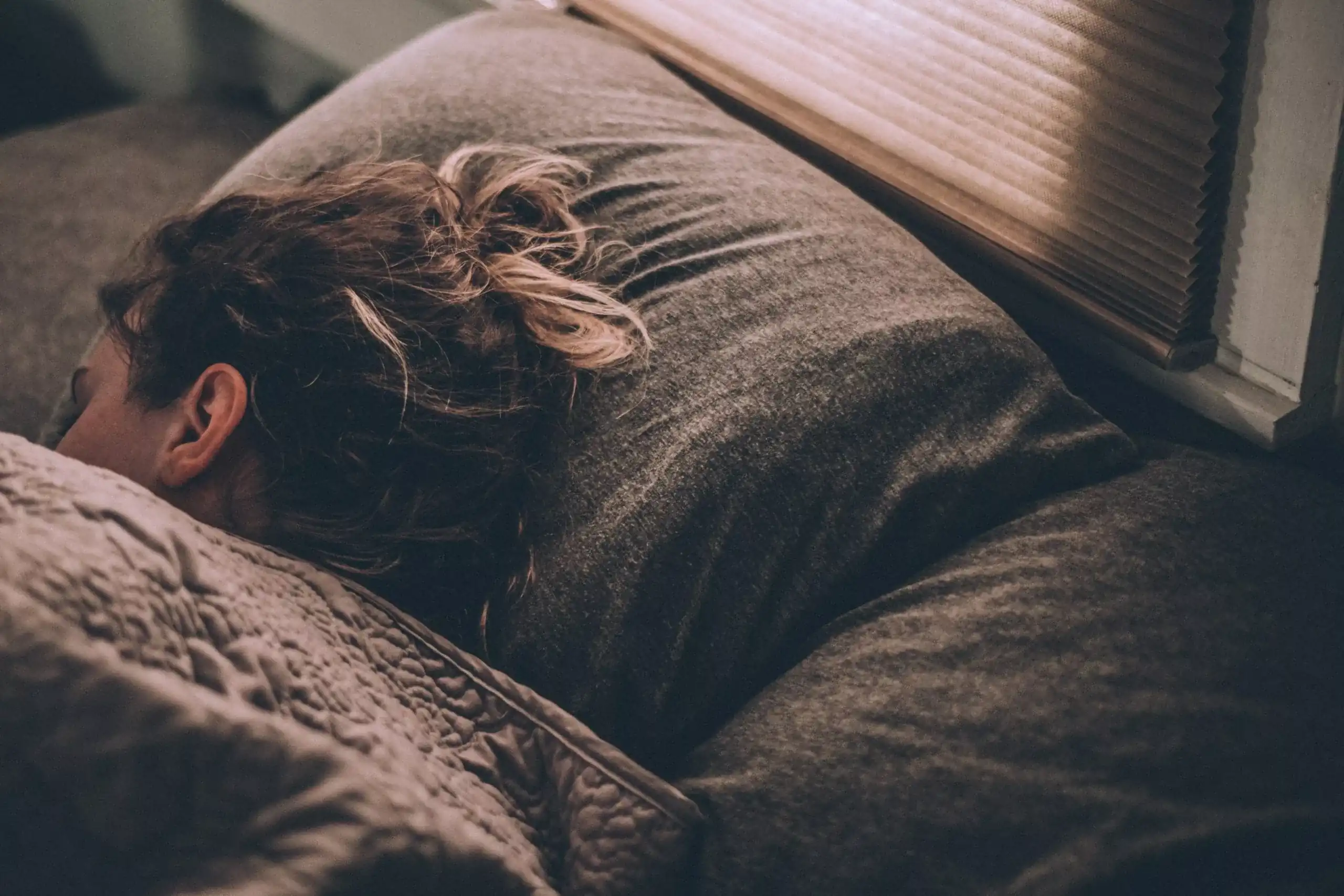 Close up of a person sleeping on a gray pillow with their head turned away from the camera