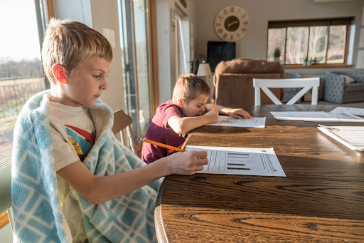 2 children seated at a wooden table holding pencils and filling out a worksheet