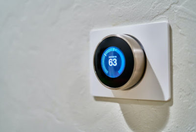 Close up of a smart thermostat set to 63 degrees against a white wall