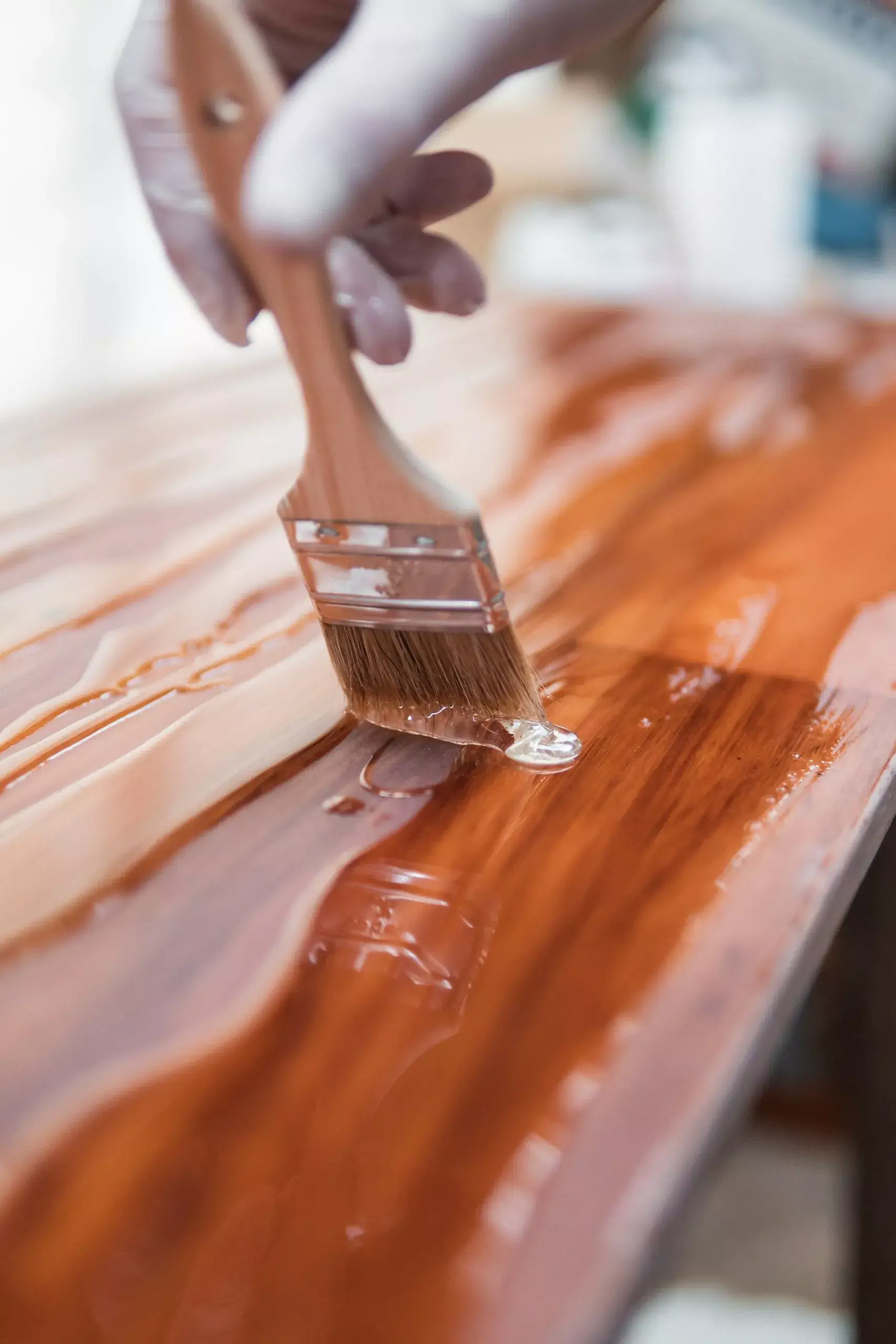 A hand adds varnish to a wooden surface with a paintbrush