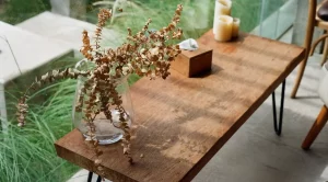 A wooden rectangular table with candles and a decorative vase on it sits in front of a large window.