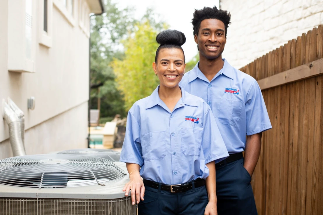 Two TemperaturePro employees smiling next to an AC condenser.
