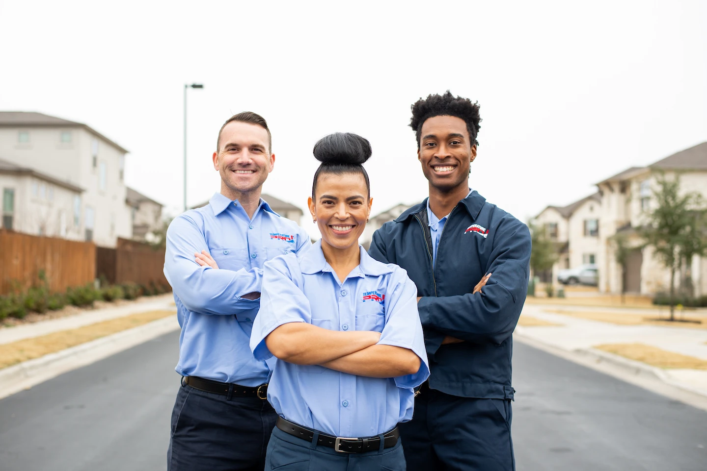 Three TemperaturePro employees smiling with arms crossed in front of a white limestone home.