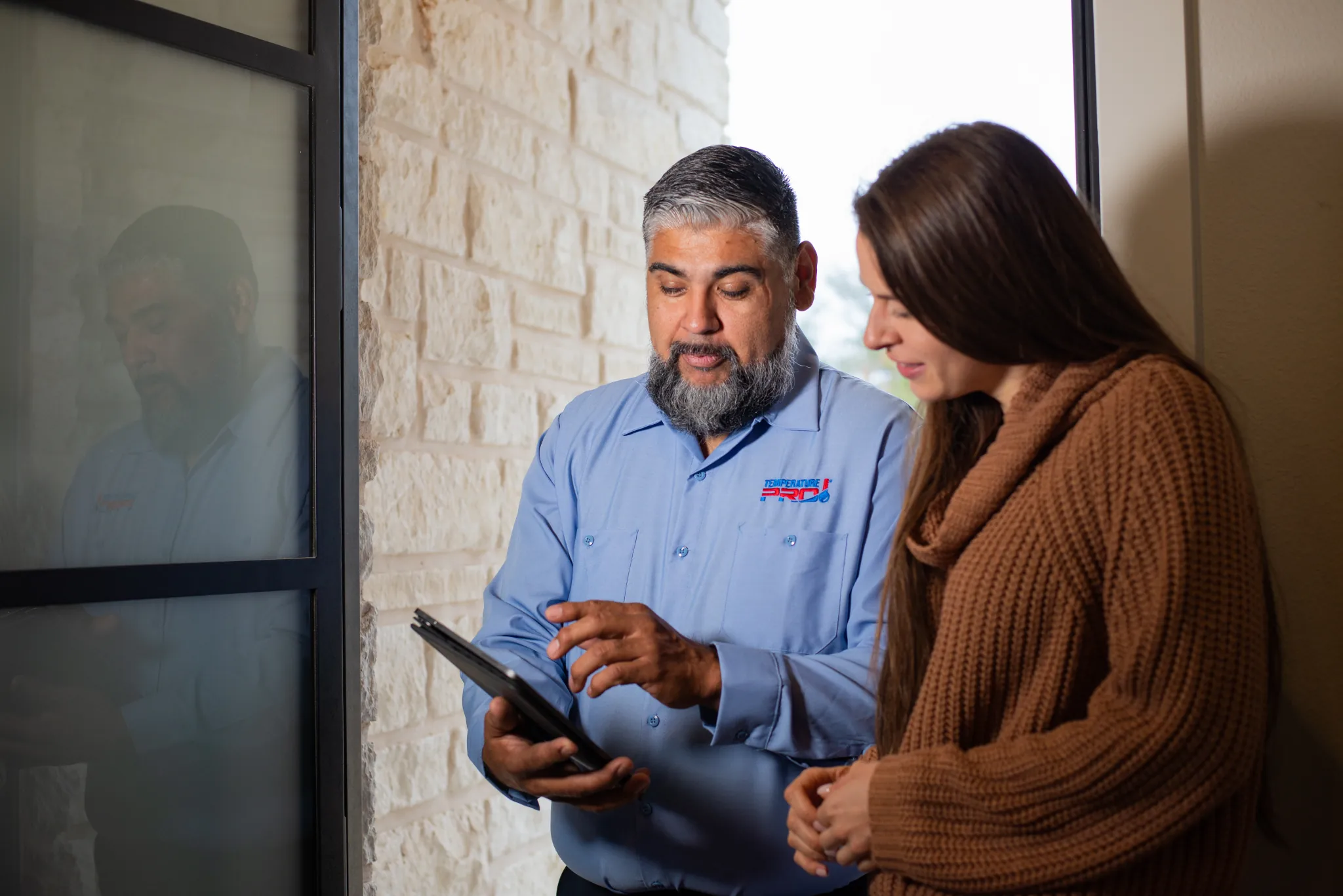 Buxmont heating technician standing with a customer at their front door, looking at an ipad.