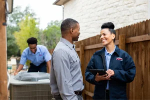 Tulsa heating technician speaking to a customer while another technician inspects the HVAC unit.