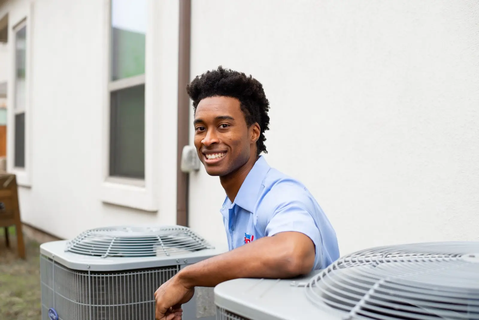 An AC repair technician from TemperaturePro sitting next to a condenser.