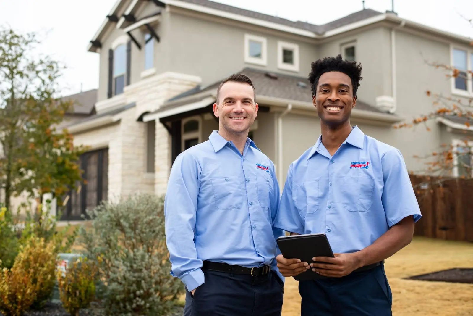 Two TemperaturePro McKinney heating service technicians in front of a home after completing a job.