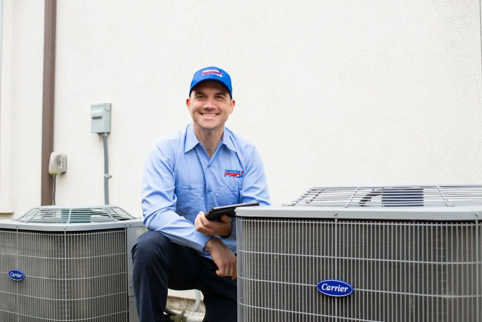 TemperaturePro heating technician kneeling next to two condensers.
