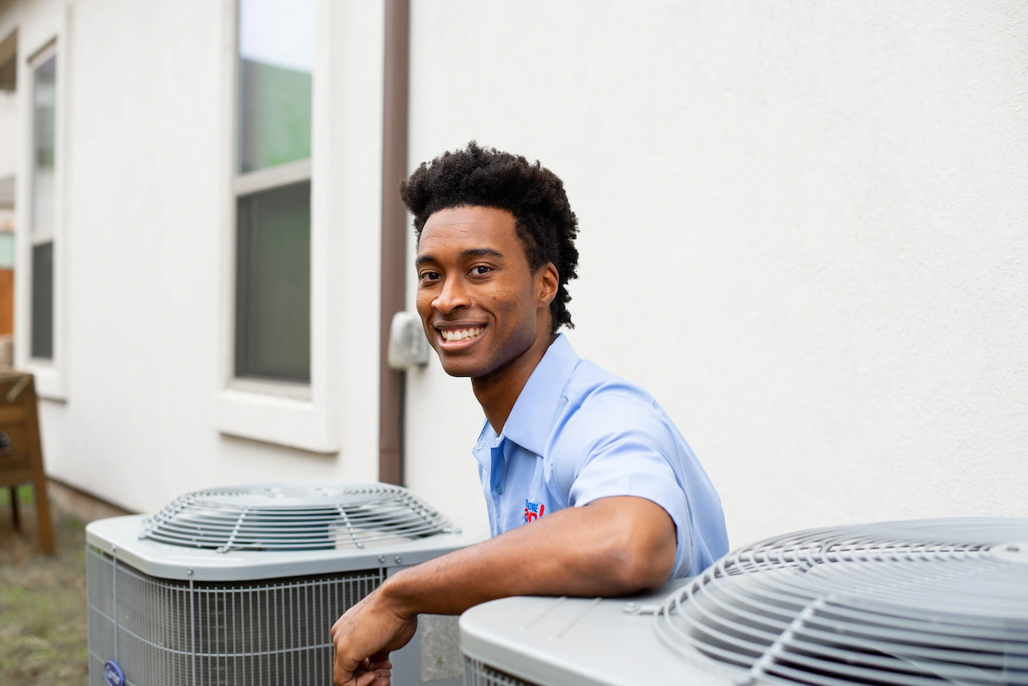 Tulsa AC technician kneeling next to AC condenser and resting arm on top of the unit.