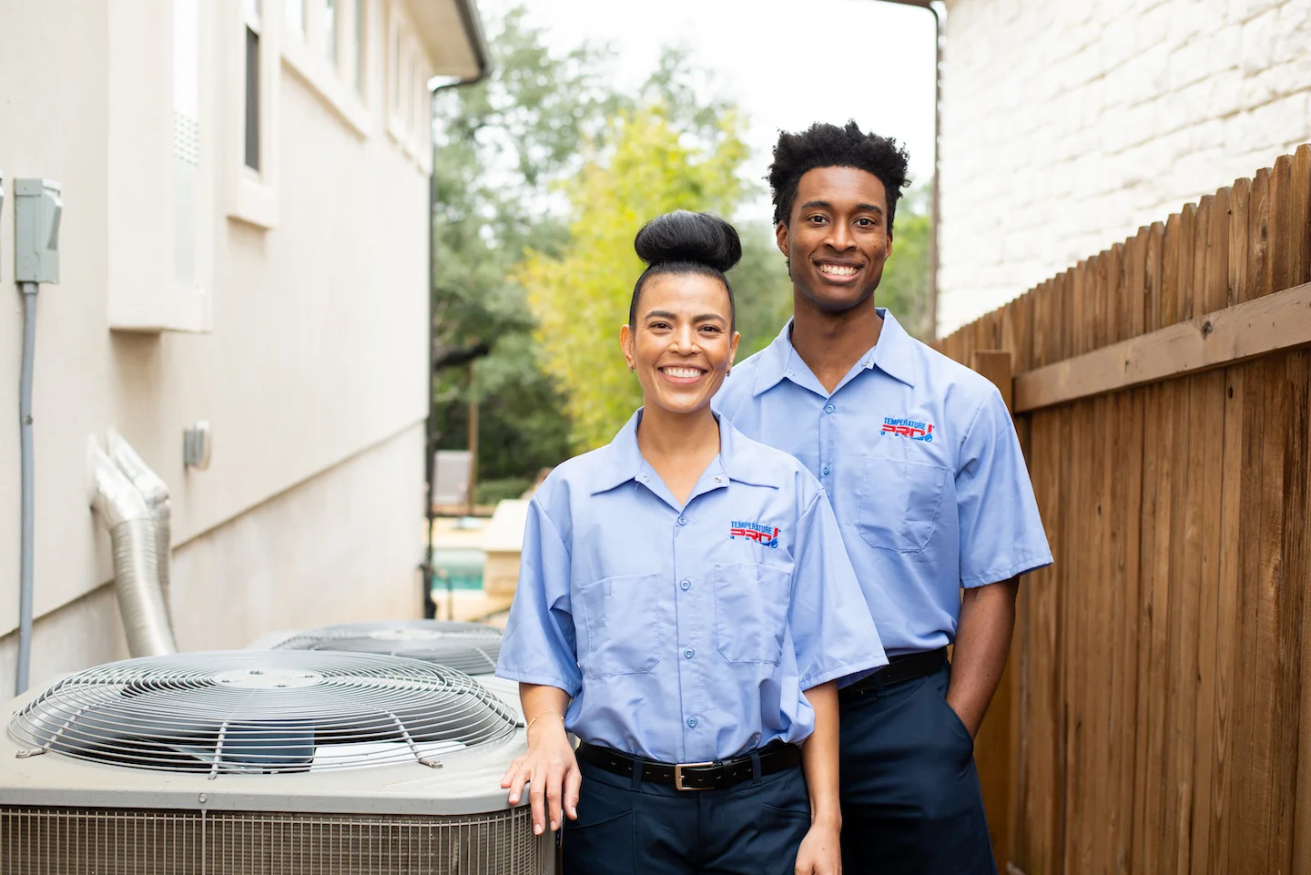 Two TemperaturePro Tulsa technicians standing side by side next to an outdoor AC condenser.