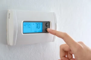 Person clicking down button on thermostat set to 70 degrees fahrenheit.