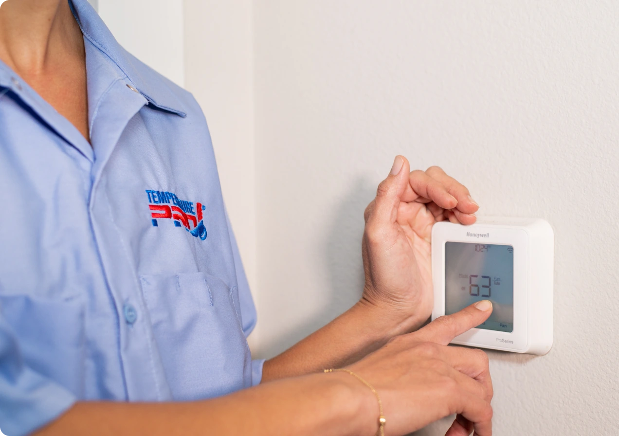 Tulsa AC maintenance technician pointing finger at thermostat set to 63 fahrenheit.