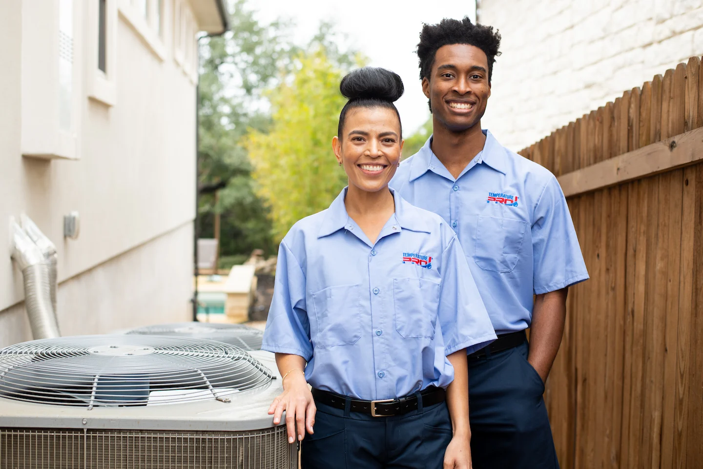 Two TemperaturePro technicians standing next to AC condenser in Tulsa backyard.