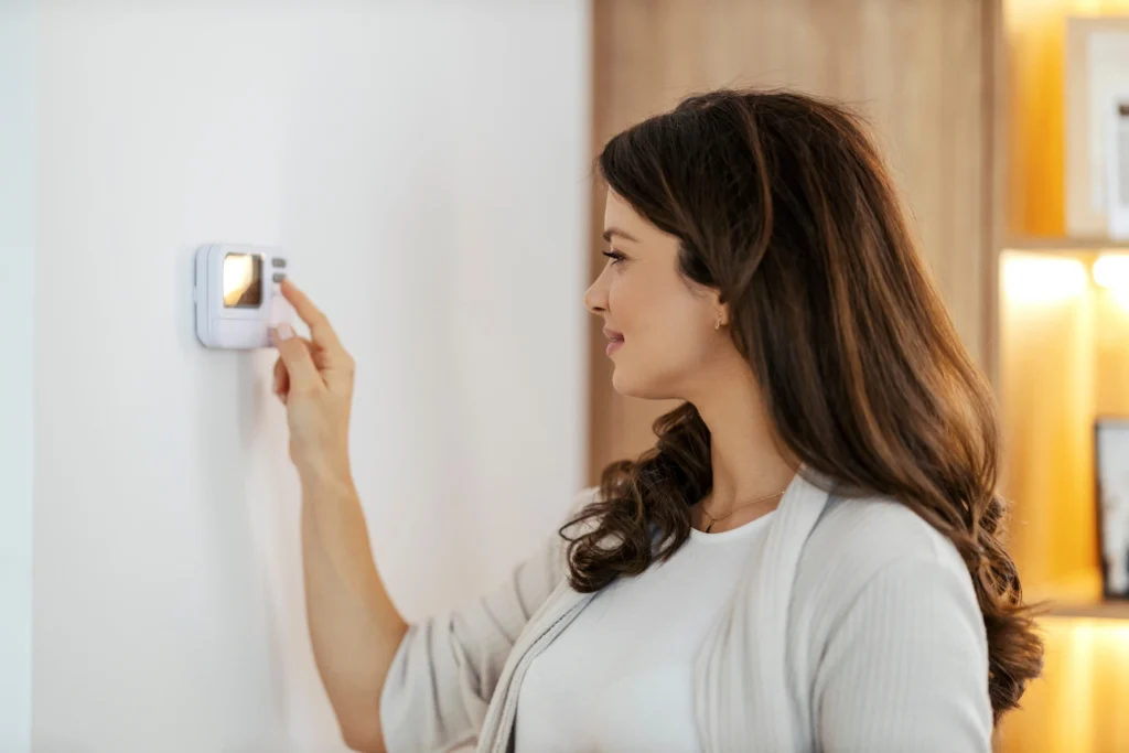 Woman adjusting thermostat after heater has been repaired.