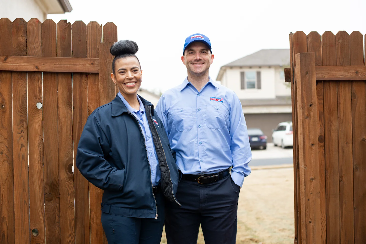 Heating installation technicians standing in between gate and smiling with hand in their pockets.