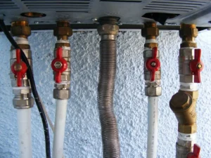 Five pipes made of plastic and metal with red handles are connected to a heating system at the top of the photo.