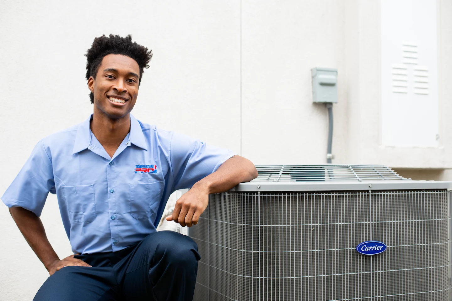 A TemperaturePro AC technician sitting next to an AC condenser.