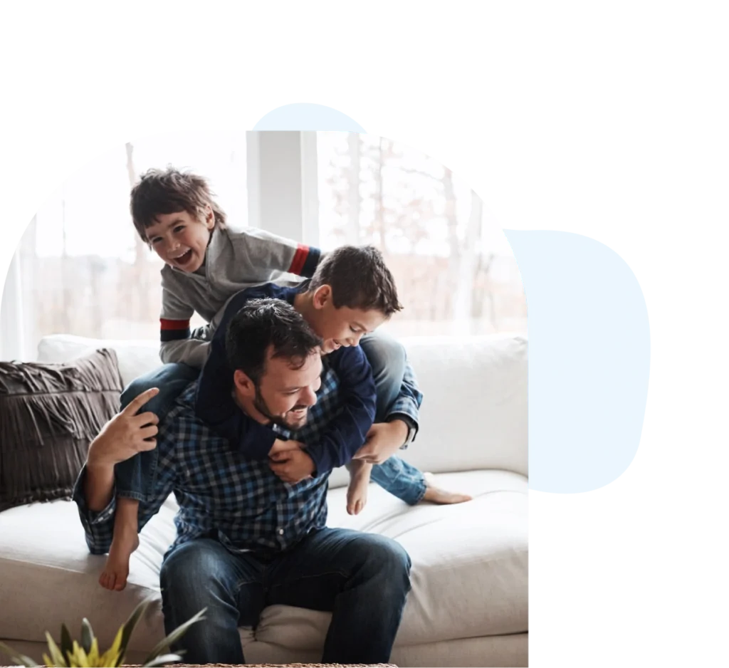 Father playing with two young sons on the couch in the living room.