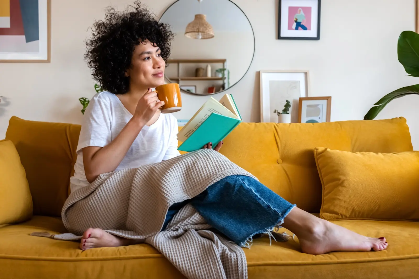 Woman sitting on couch with book and mug.