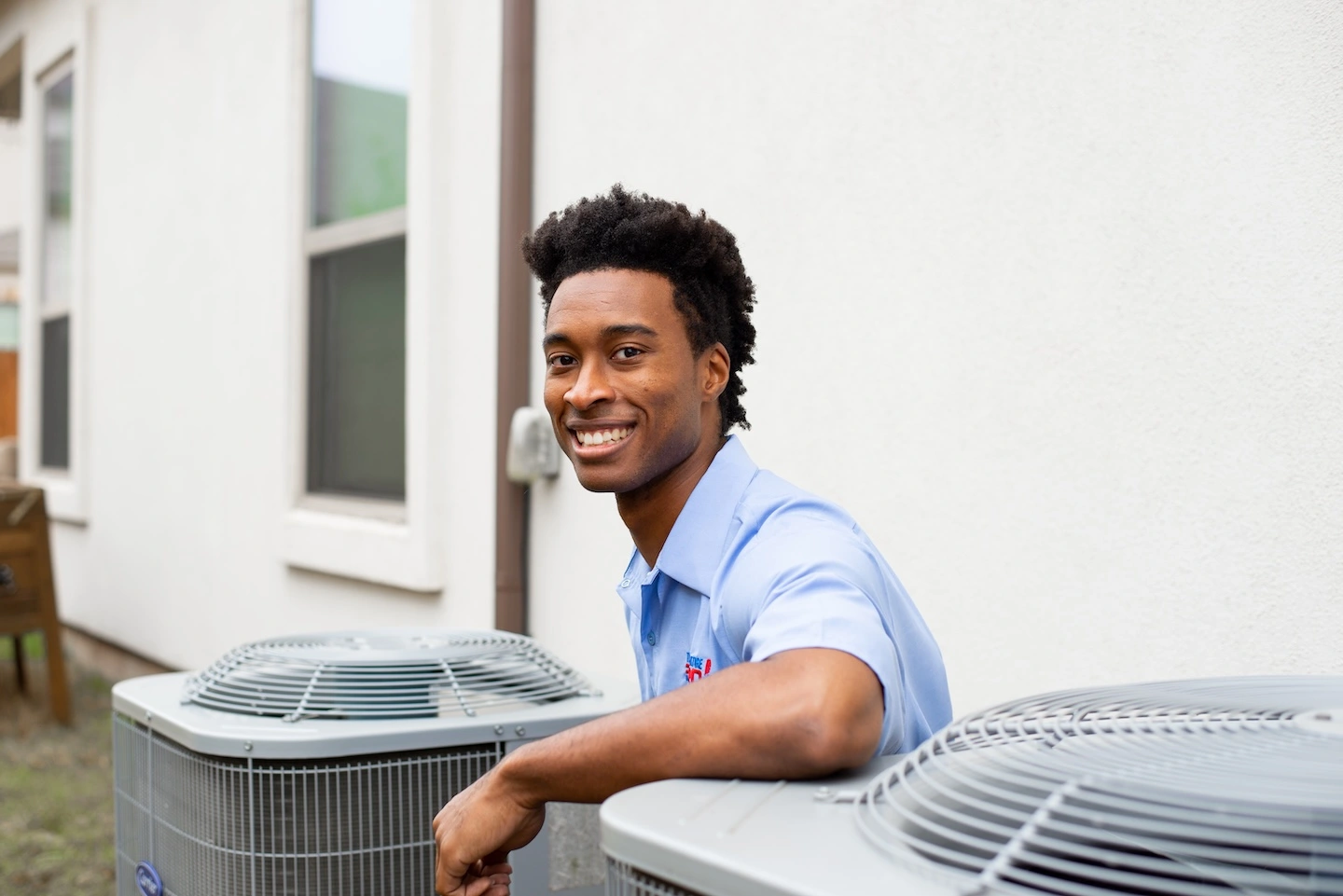 A Kalamazoo AC repair technician is shown kneeling next to a condenser unit, resting an arm on top of it.