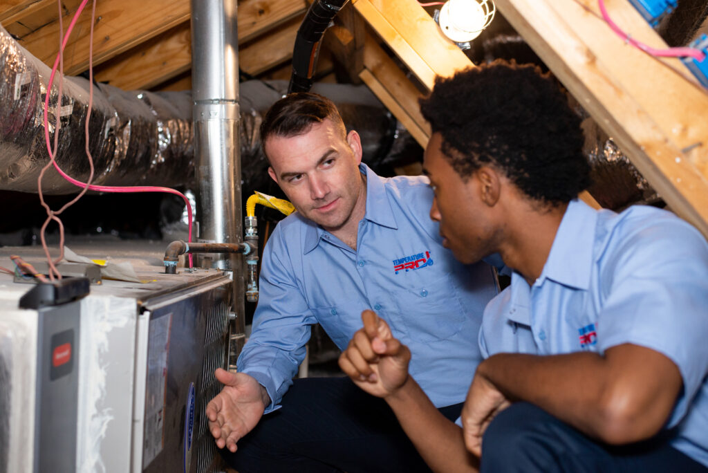 Two HVAC technicians in Silicon Valley assess a unit inside of the attic.