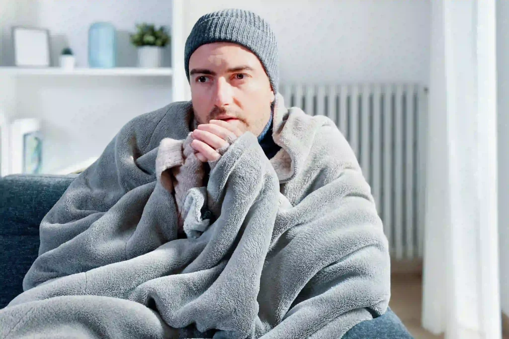 Man bundled in blanket and hand warmers waiting for furnace repair technician.