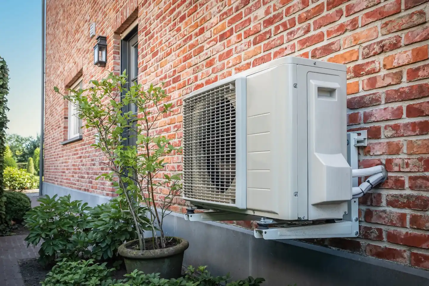 A heat pump installed on the side of a brick home. 