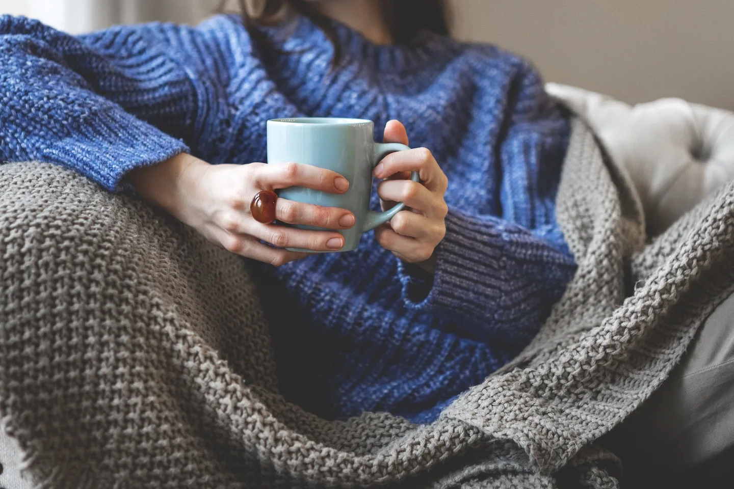 A woman relaxes with a warm drink and blankets at home in the winter.